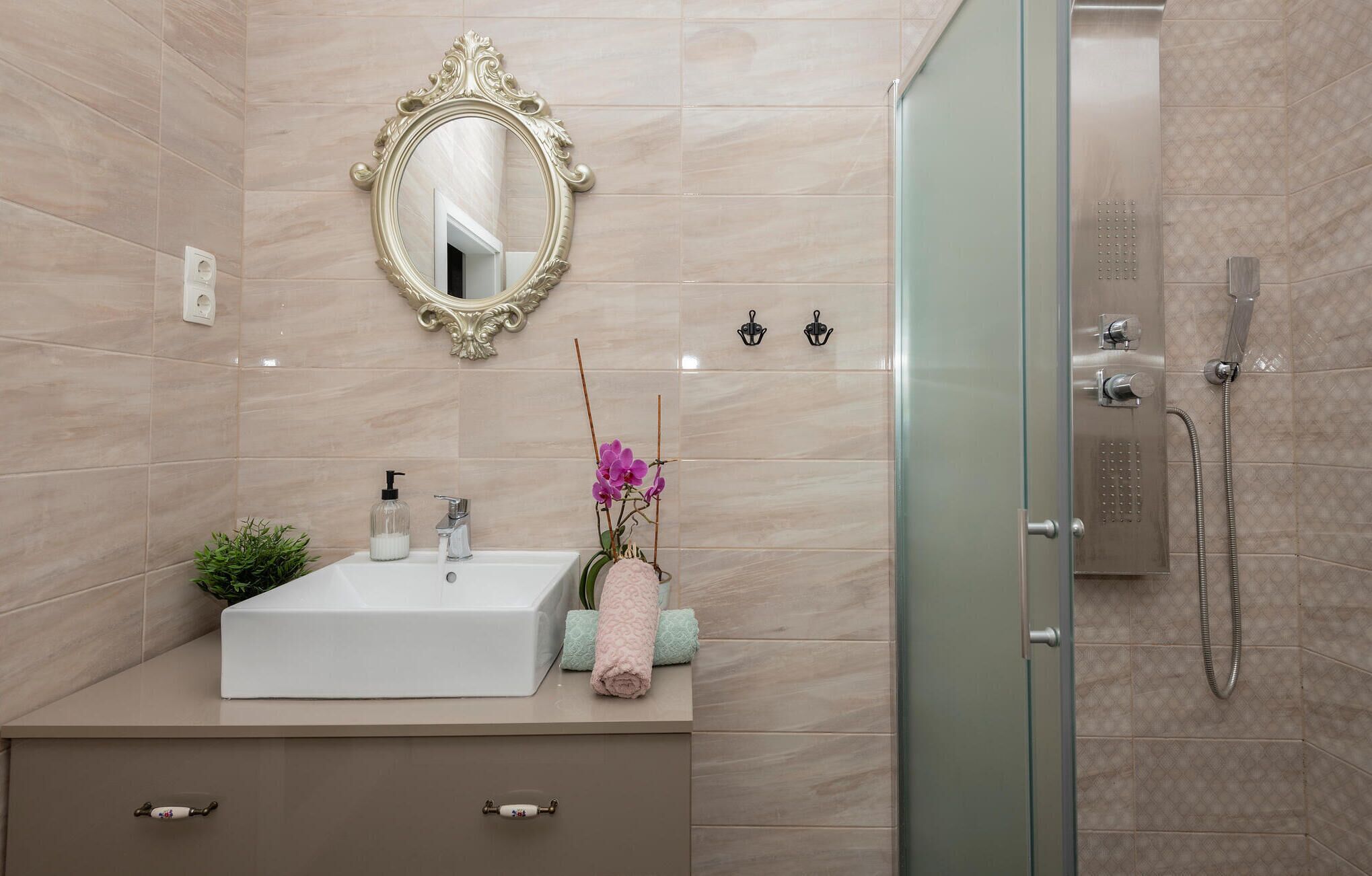 Un bagno con un lavandino bianco, uno specchio, una cabina doccia in vetro e un'orchidea in vaso.