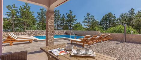A rooftop pool area with lounge chairs, a table with magazines and drinks, and a stone wall.