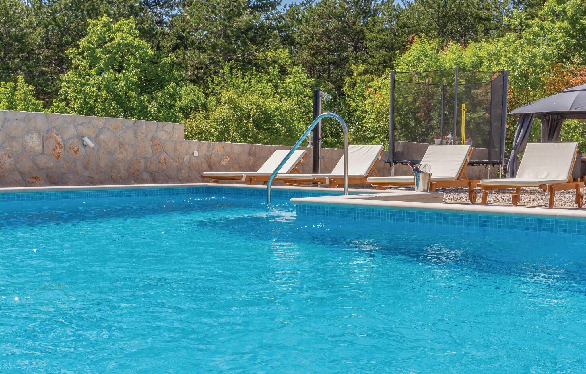 A swimming pool with clear blue water, surrounded by lounge chairs and a stone wall.