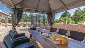 An outdoor dining area with a covered table, wicker chairs, and a stone wall backdrop. - Amazing home in Imotski (Imotski)