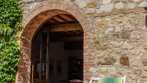 A stone building with an arched doorway, a green chair, and potted plants. - Luxury converted barn with hilltop views in chianti wine region, Tuscany (Castellina in Chianti)