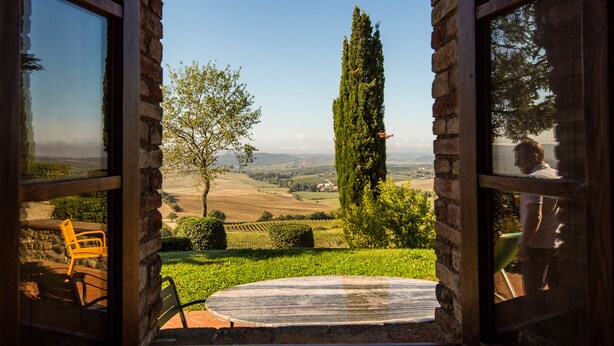A room with a large window offering a view of a garden, a tall tree, and a distant landscape. - Luxury converted barn with hilltop views in chianti wine region, Tuscany (Castellina in Chianti)