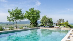 A clear swimming pool with lounge chairs and a pergola, surrounded by trees and a view of the countryside. - Luxury converted barn with hilltop views in chianti wine region, Tuscany (Castellina in Chianti)