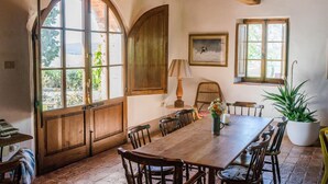 A rustic dining area with a wooden table and chairs, large windows, and a view of greenery. - Luxury converted barn with hilltop views in chianti wine region, Tuscany (Castellina in Chianti)