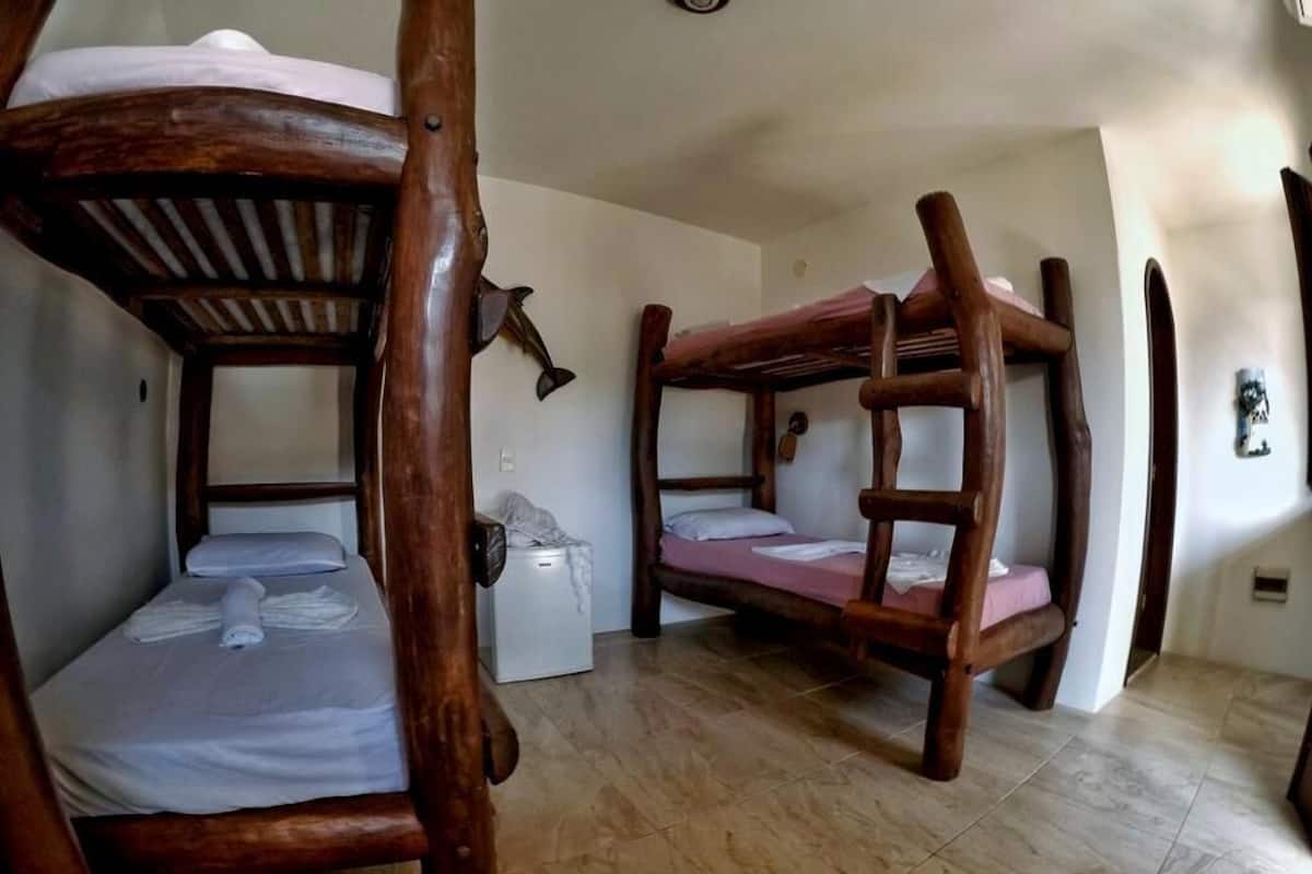 A room with two bunk beds made of wood, a small white appliance, and a wall-mounted fan.