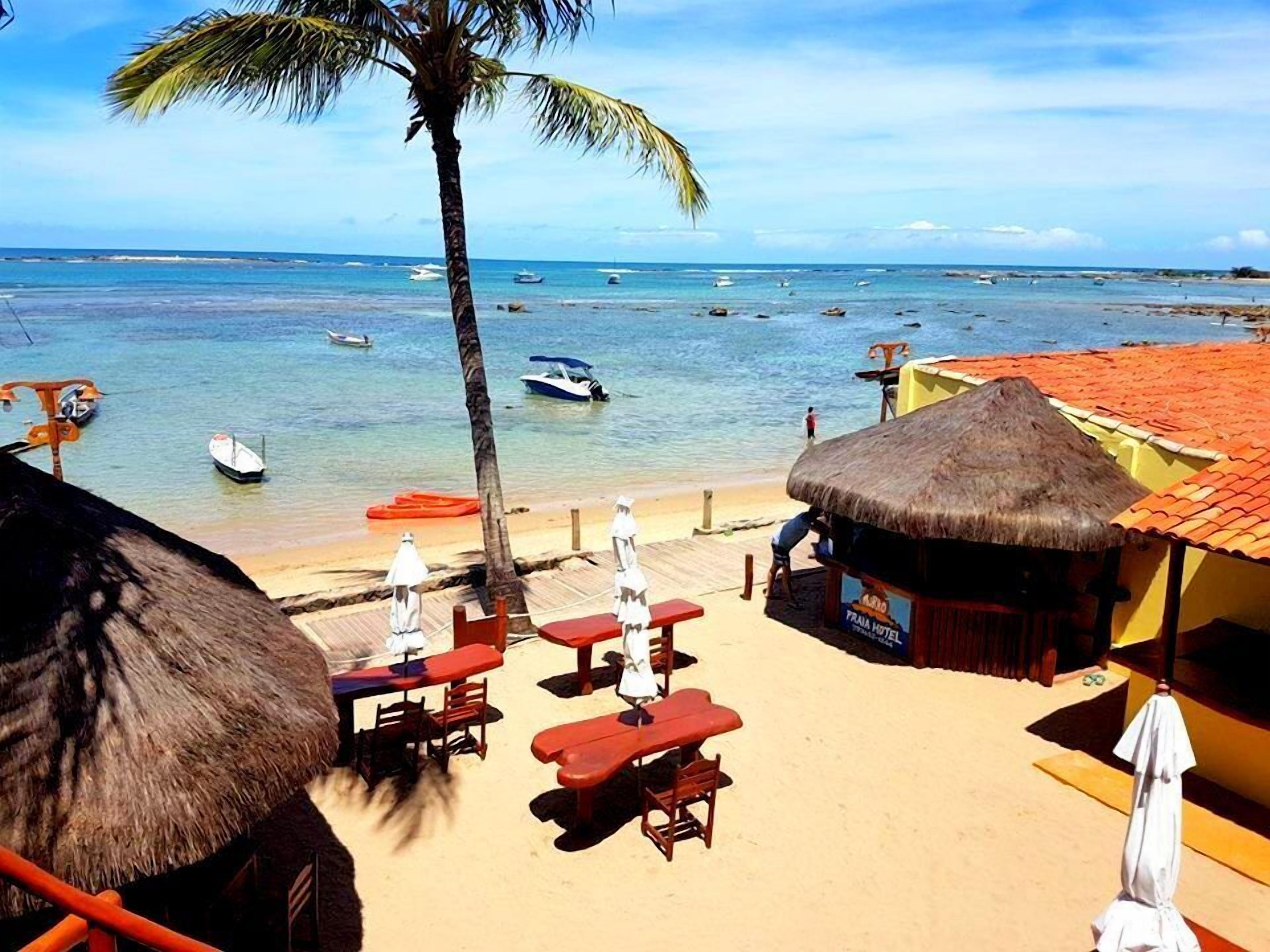 A beachside view with a thatched-roof hut, red benches, and a visible 'Frau Hotel' sign.