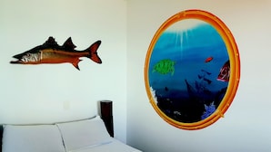 Un dormitorio con cama, un adorno de pez en la pared y un acuario redondo con peces y un barco.