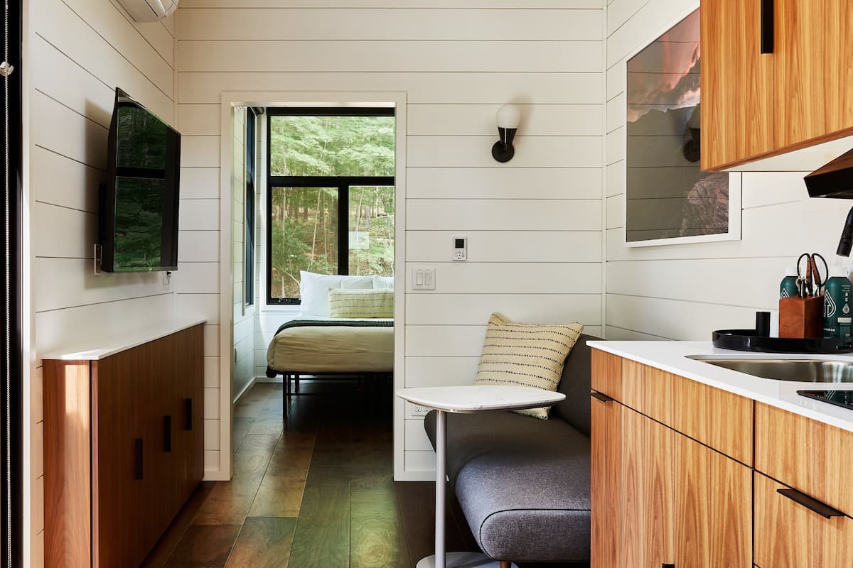 A compact kitchen with wooden cabinets, a built-in stove, and a window overlooking a forest.