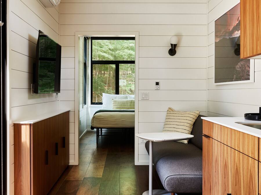 Une cuisine compacte avec des meubles de rangement en bois, une cuisinière intégrée et une fenêtre donnant sur une forêt.