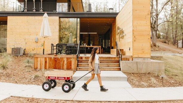 A modern wooden house with a large glass door, a wooden deck, and a small cart. - AutoCamp Yosemite (Mariposa)