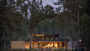 A modern two-story house with a large open patio area, surrounded by a forest and a body of water. - AutoCamp Yosemite (Mariposa)