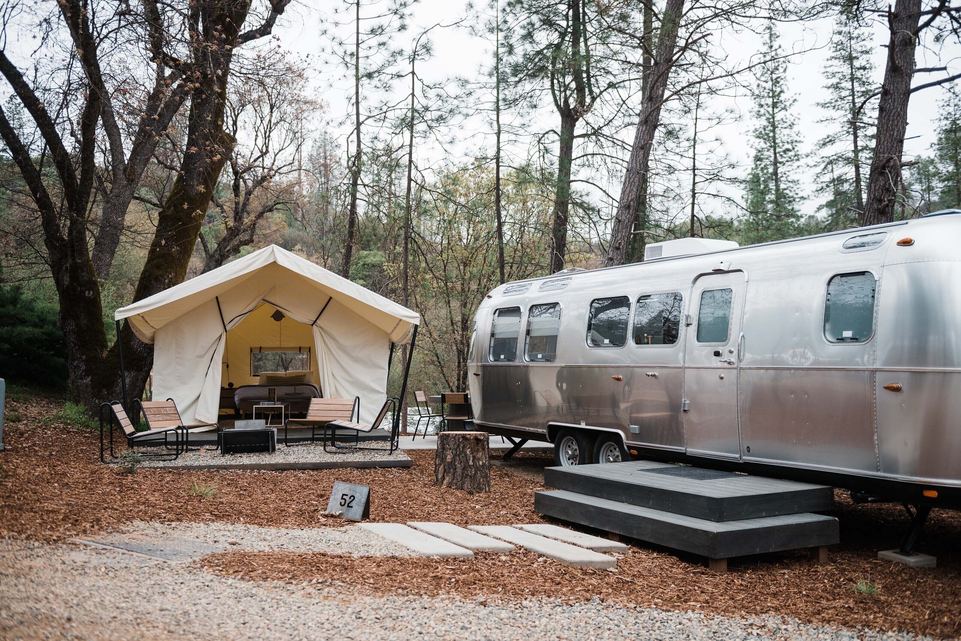 A campsite with a tent and a trailer. There are steps leading to the trailer, and a number '52' sign is visible.