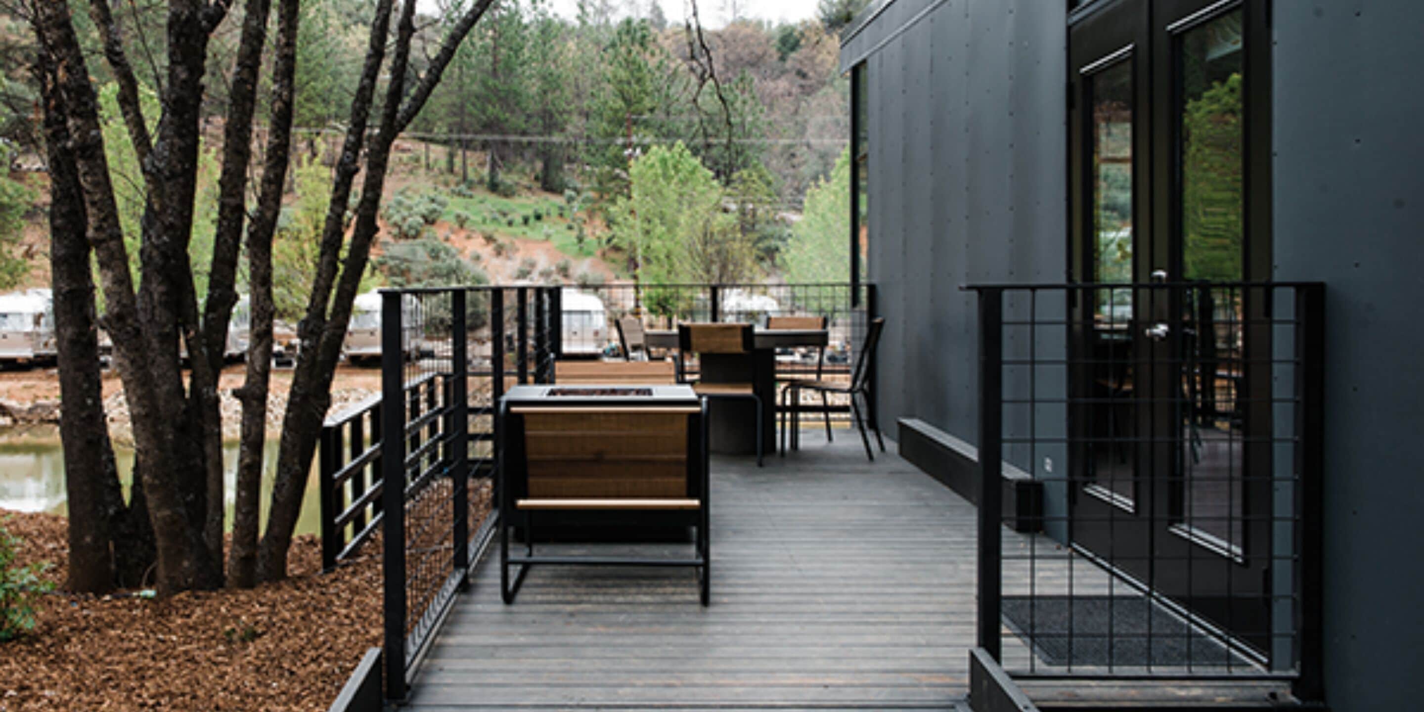 A wooden deck with a bench and table, surrounded by trees and a view of a hilly landscape.