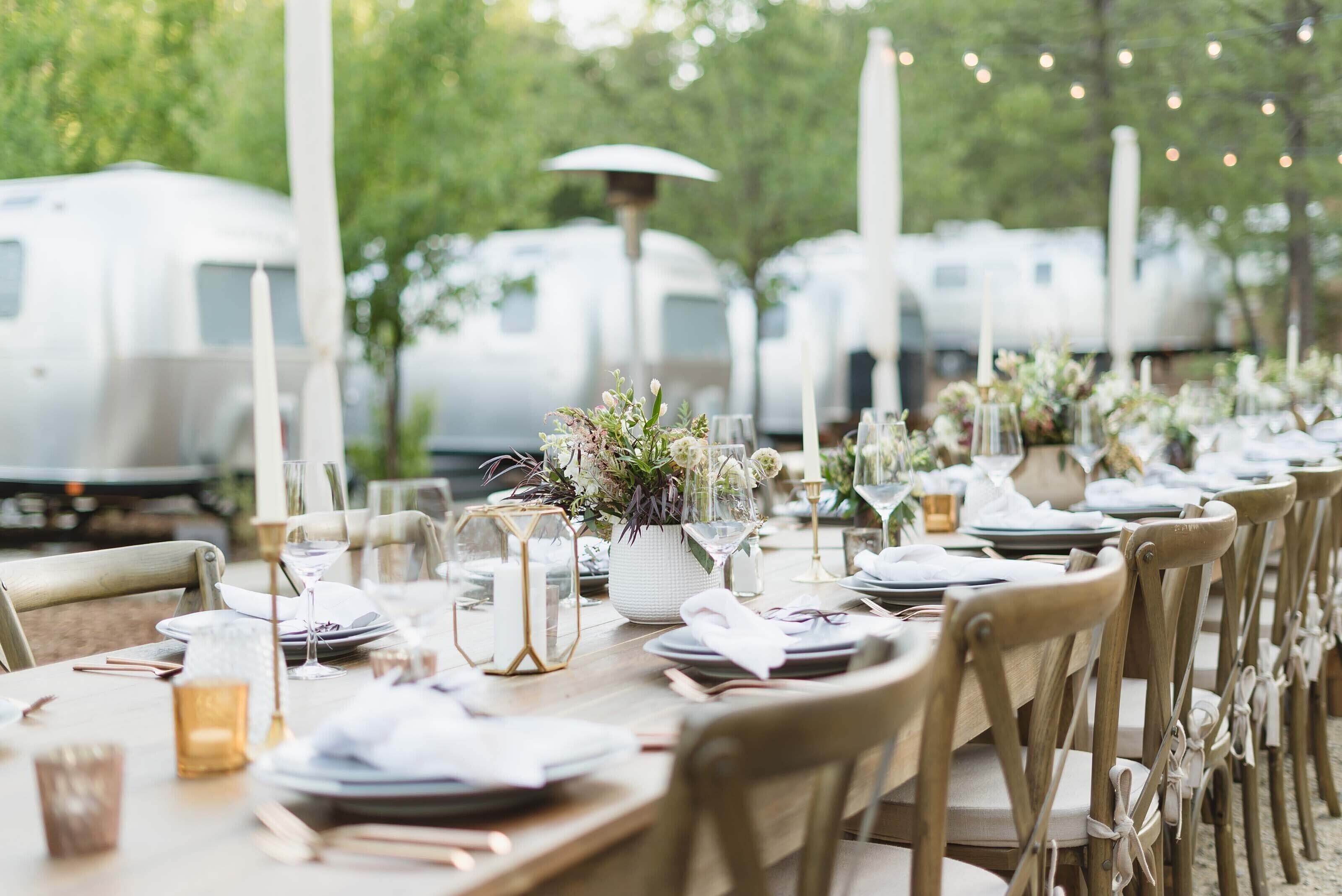 A long dining table set for a formal event with white tablecloths, glassware, and floral centerpieces.