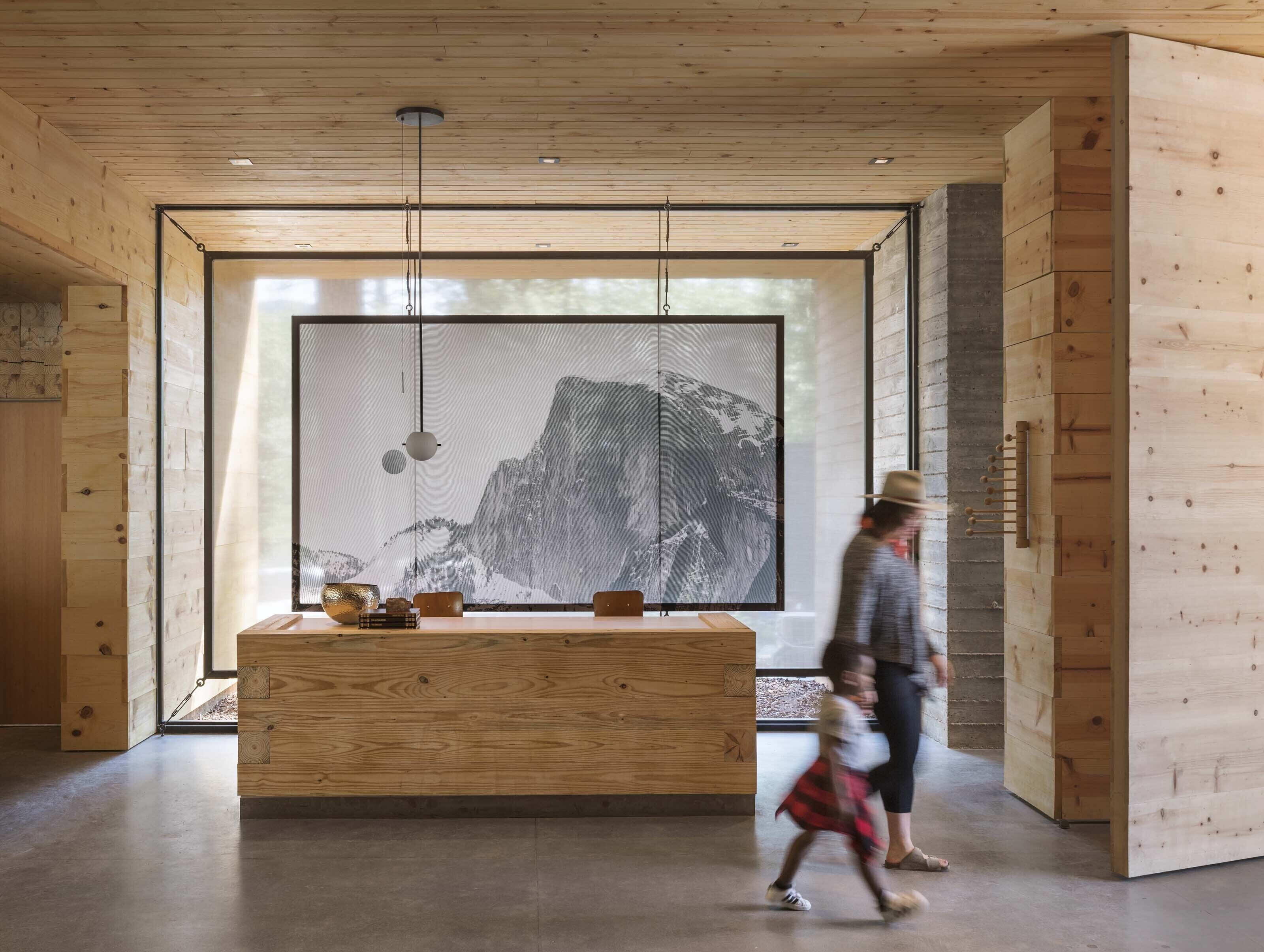 A modern interior with a wooden reception desk, a large window with a view of a mountain, and a hanging light fixture.