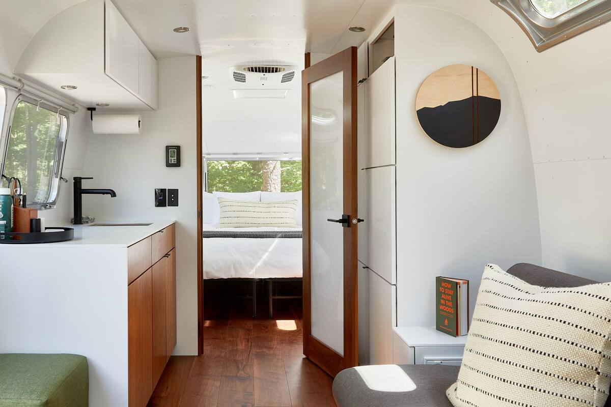 A compact RV interior with a kitchenette, a bed, and a small seating area.