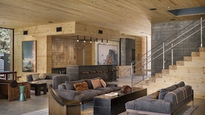 A modern living room with a large sectional sofa, a coffee table, and a staircase leading to an upper level. - AutoCamp Yosemite (Mariposa)