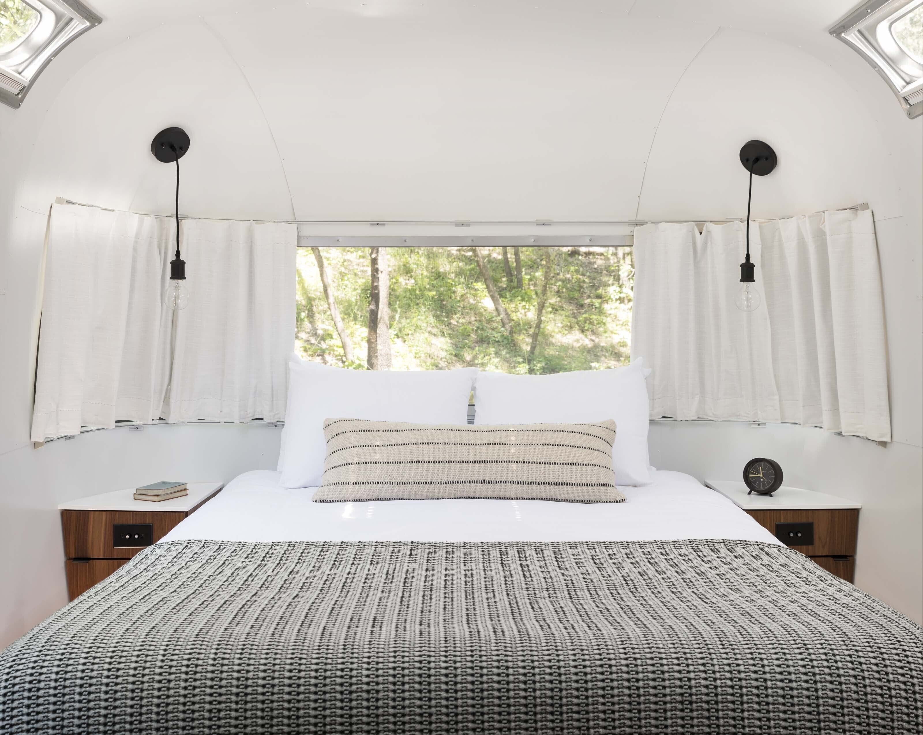 Una camera da letto con un letto grande, tende bianche e vista sugli alberi attraverso una finestra.