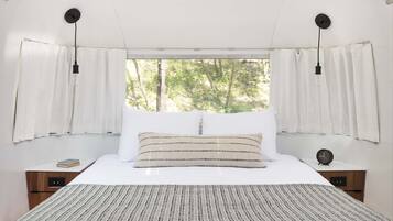 Una camera da letto con un letto grande, tende bianche e vista sugli alberi attraverso una finestra.