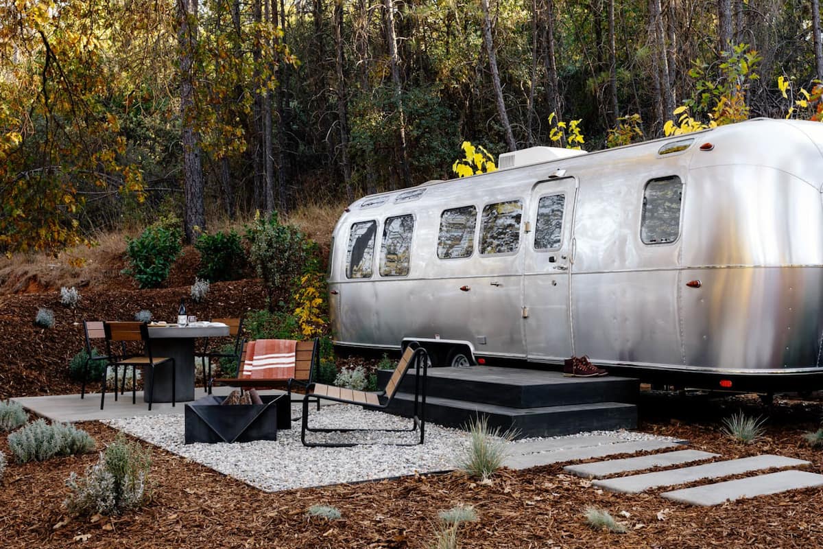 A vintage trailer with a table and chairs set up in a garden area.