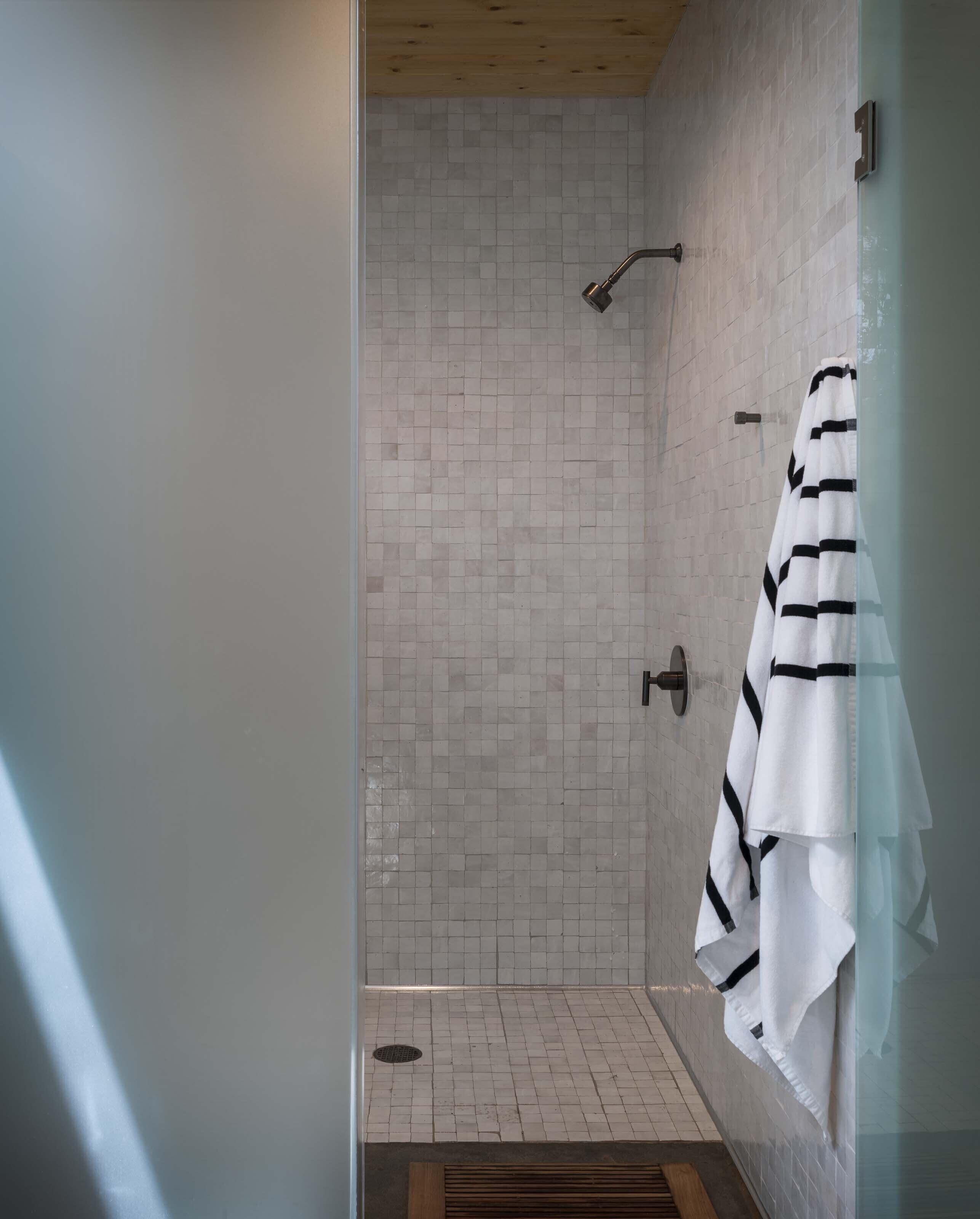 A modern shower with a tiled wall, a wooden ceiling, and a striped towel hanging on the wall.