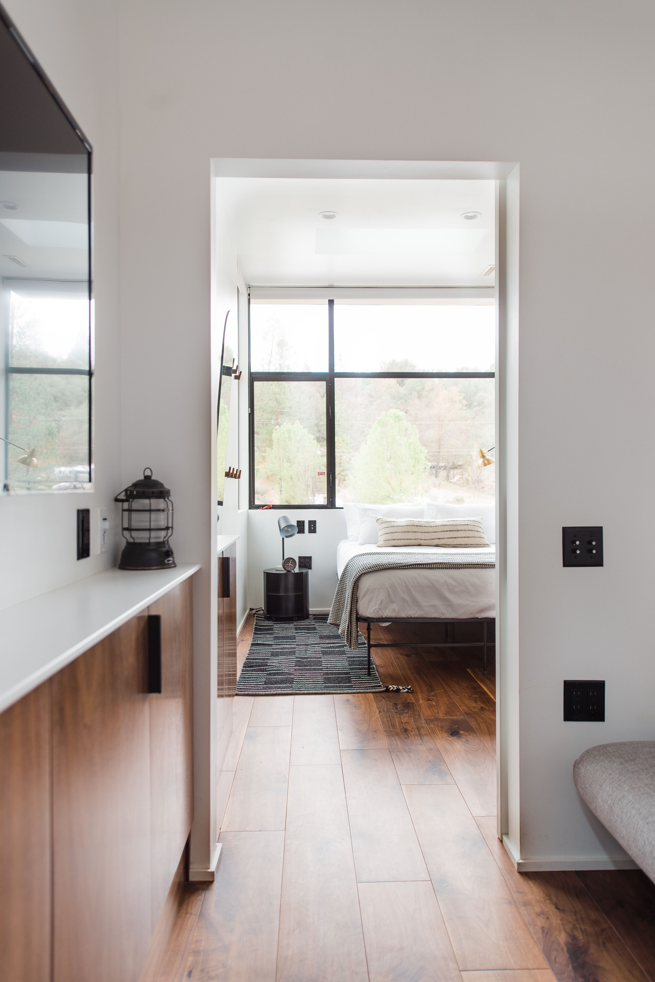 Quarto moderno com uma janela grande, uma cama, uma mesa de cabeceira e um abajur.
