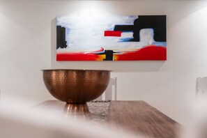 A modern interior with a minimalist design, featuring a large abstract painting on the wall and a copper bowl on a wooden table. - Eden on the Bay 108 (Cape Town)