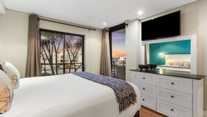 A hotel room with a bed, a TV, a balcony with a view, and a white dresser. - Eden on the Bay 108 (Cape Town)