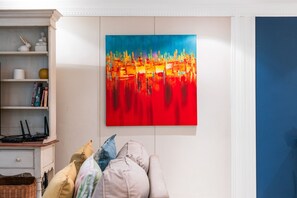 Une pièce avec un mur blanc, une bibliothèque, un téléviseur à écran plat et un tableau abstrait aux couleurs vives.