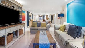 A modern living room with a flat-screen TV, sofas, a coffee table, and a dining area in the background. - Eden on the Bay 108 (Cape Town)