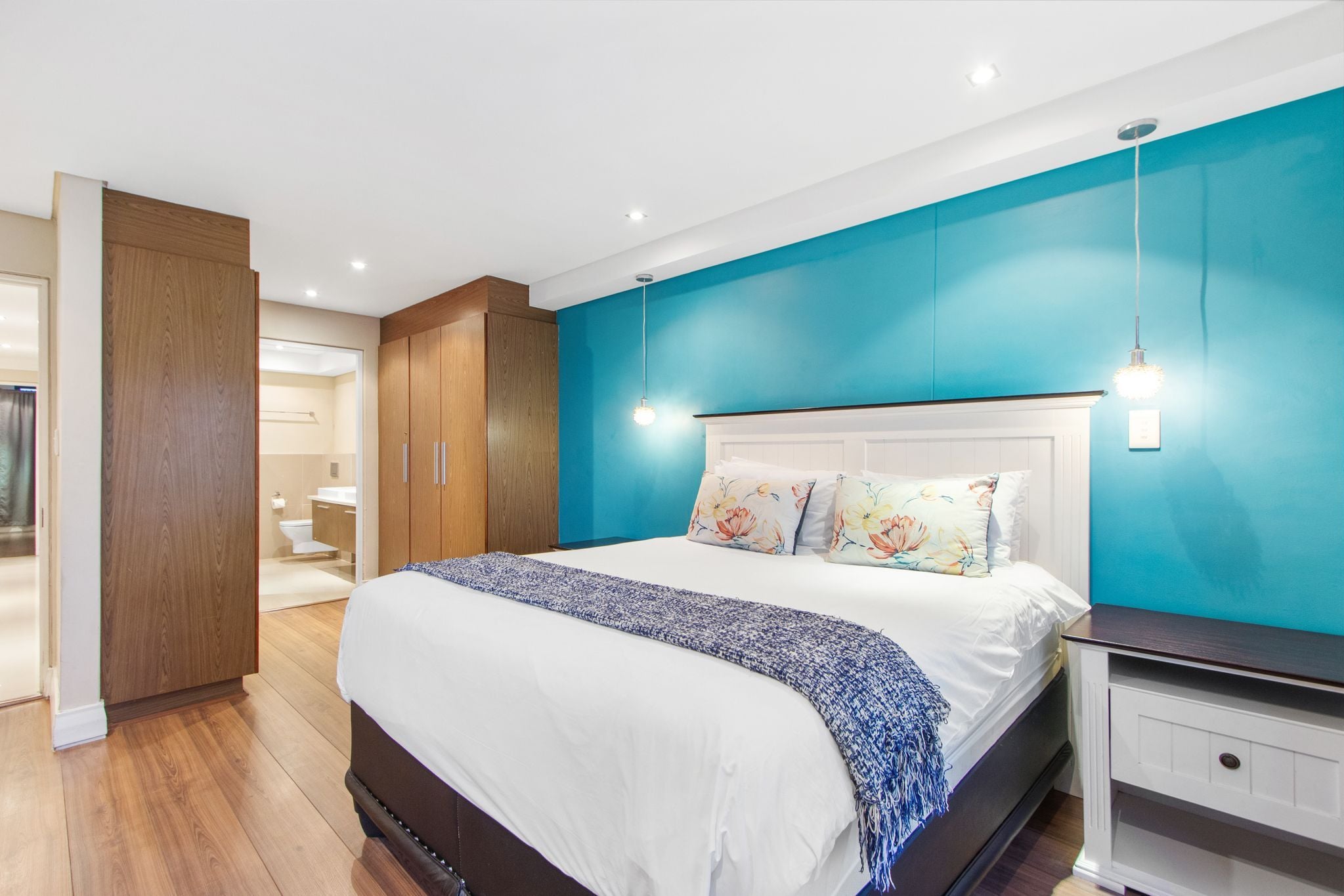Un dormitorio moderno con una cama grande, un armario de madera y un baño visible a través de una puerta abierta.