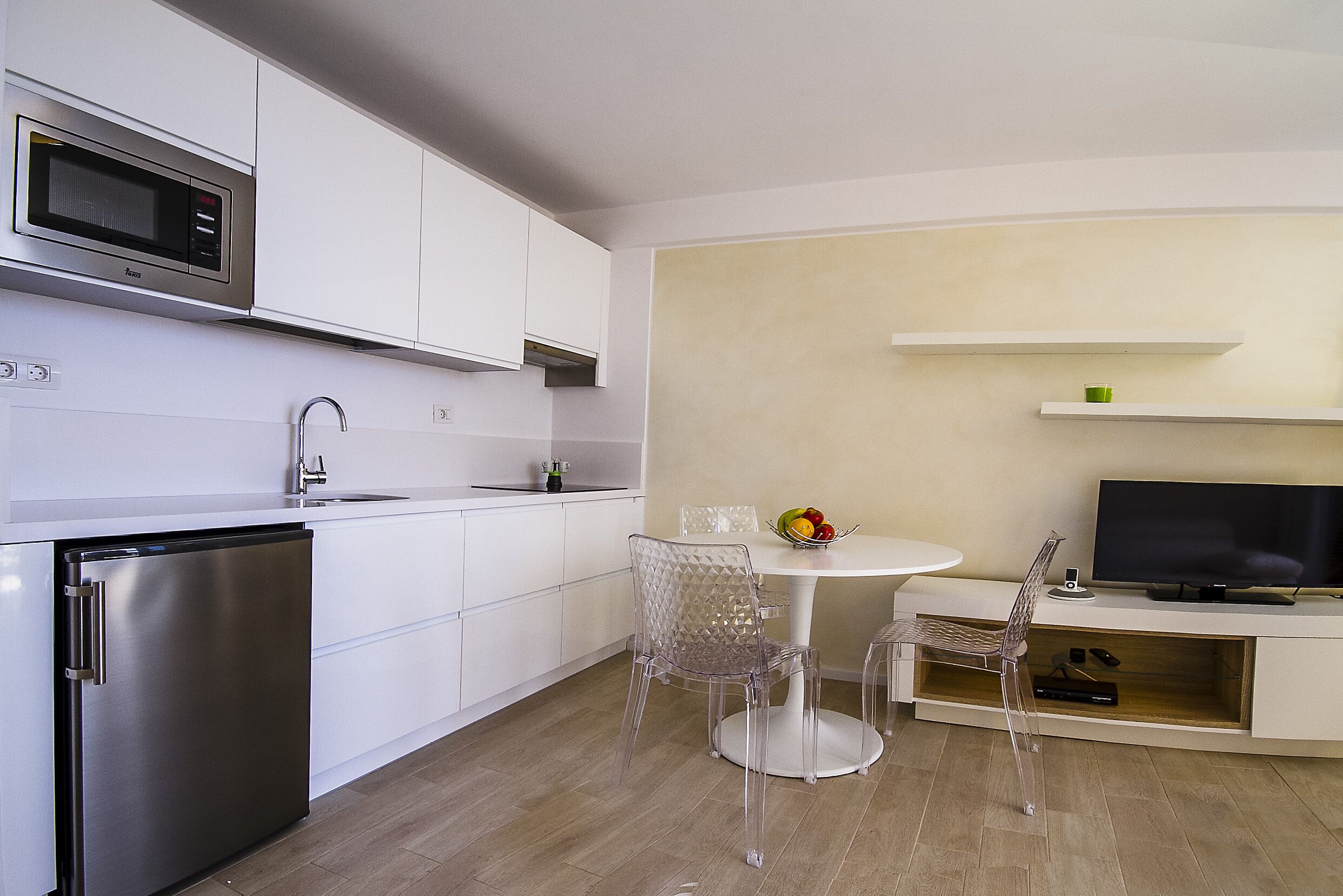 A modern kitchen with a built-in microwave, a refrigerator, and a dining area with a table and chairs.