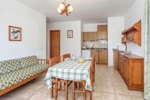 A dining area with a table set for four, a wooden cabinet, and a kitchen in the background.
