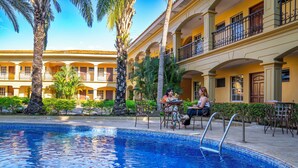 A pool area with a clear blue pool, surrounded by palm trees and a building with balconies. - Hotel Florencia San Miguel (San Miguel)