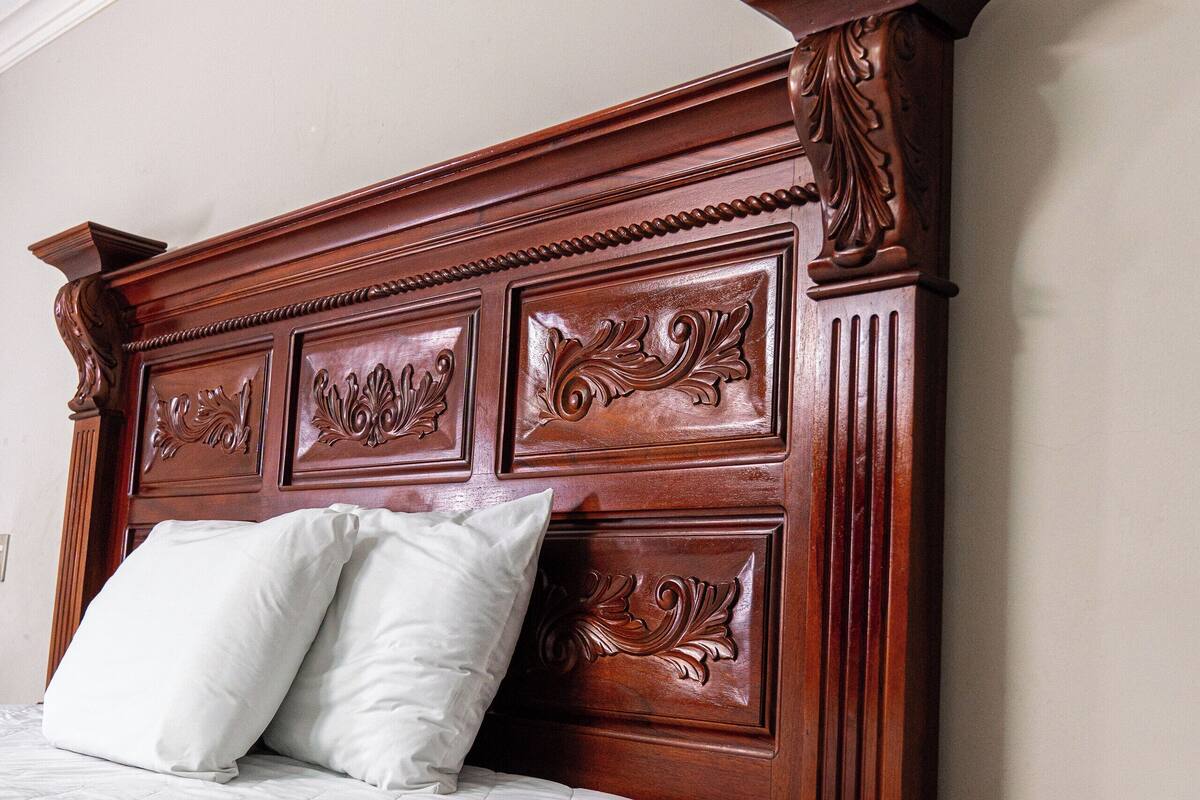 Una cama de madera con cabecera, dos almohadas y una mesita de noche con lámpara.