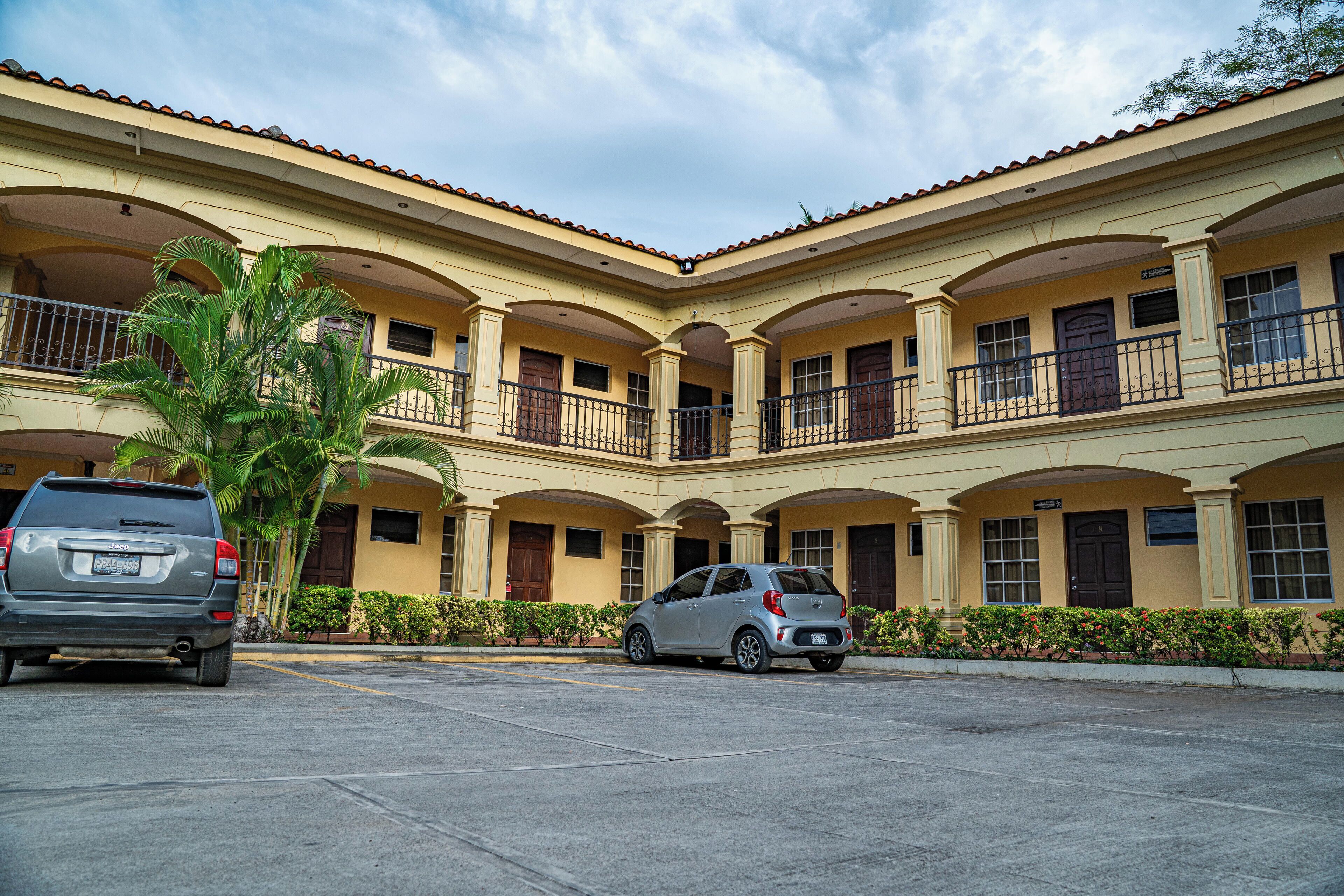 A multi-story building with a courtyard, featuring balconies and a parking area with two cars.