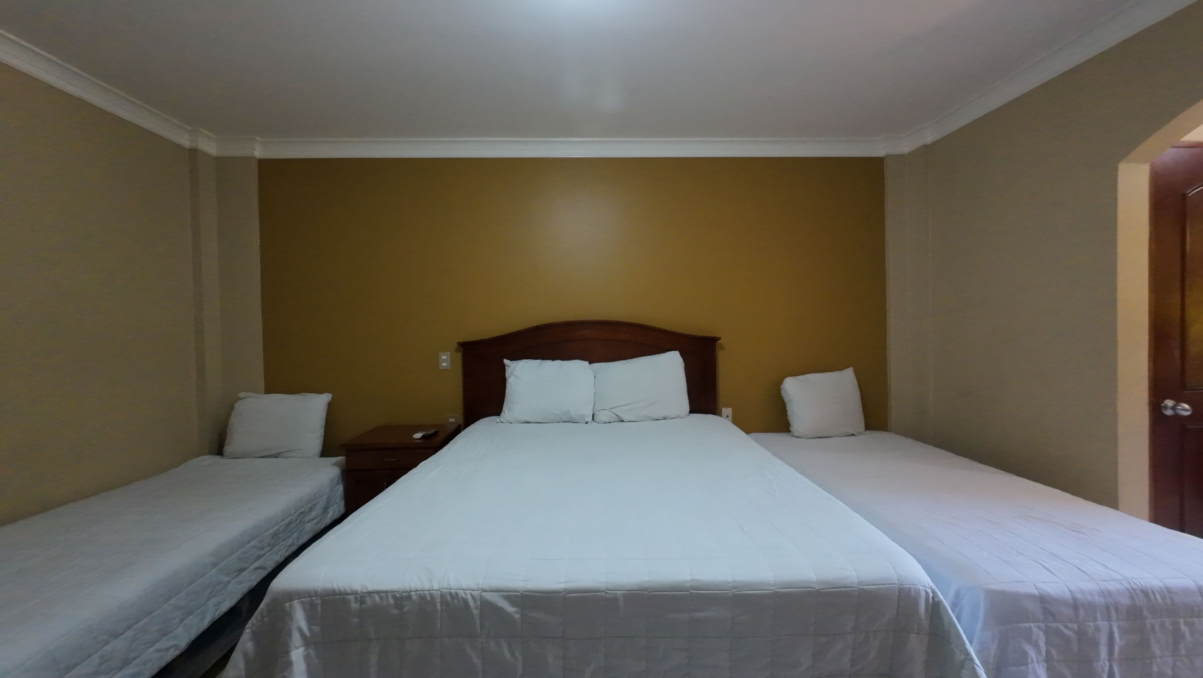 A room with two single beds, a wooden headboard, and a nightstand with a remote control.