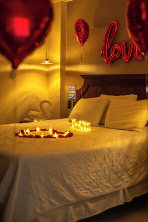 Une chambre d’hôtel avec un lit, une serviette pliée en forme de cygne et des ballons rouges formant le mot « amour ».
