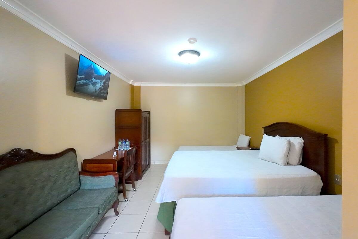Una habitación de hotel con dos camas, un sofá, un televisor y un armario.