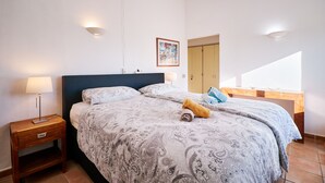 A bedroom with a bed, bedside table, lamp, and a painting on the wall. - Apartment Kornelius (Carvoeiro)