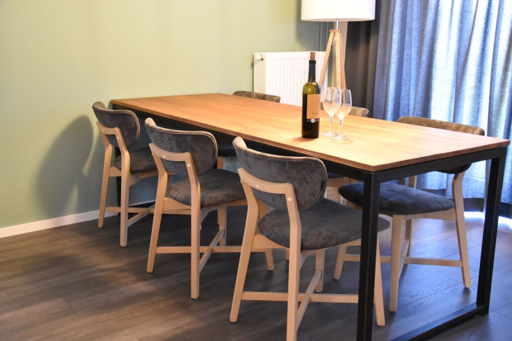 Een eethoek met een houten tafel en vier stoelen, een fles wijn en een glas op de tafel.