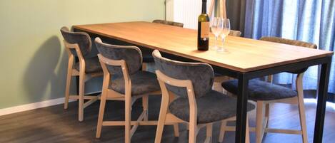Een eethoek met een houten tafel en vier stoelen, een fles wijn en een glas op de tafel.