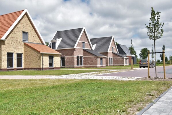 Une rangée de maisons modernes, dotées de toits à pignon et de façades en briques, avec une allée pavée et une pelouse agrémentée de jeunes arbres.