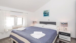 Une chambre à coucher avec un lit, une table de chevet, une fenêtre avec des rideaux et un tableau au mur.