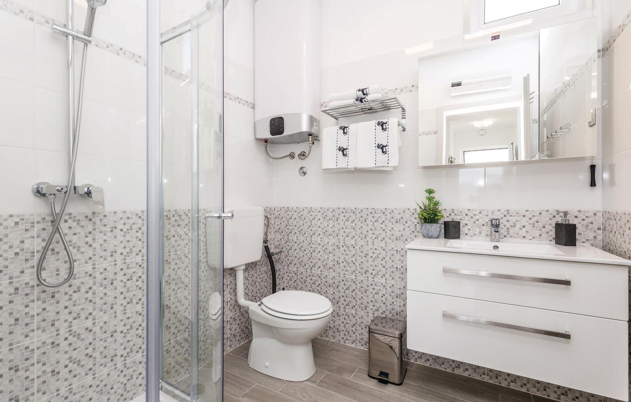 A modern bathroom with a glass shower enclosure, a toilet, a sink with a mirror, and a small trash bin.