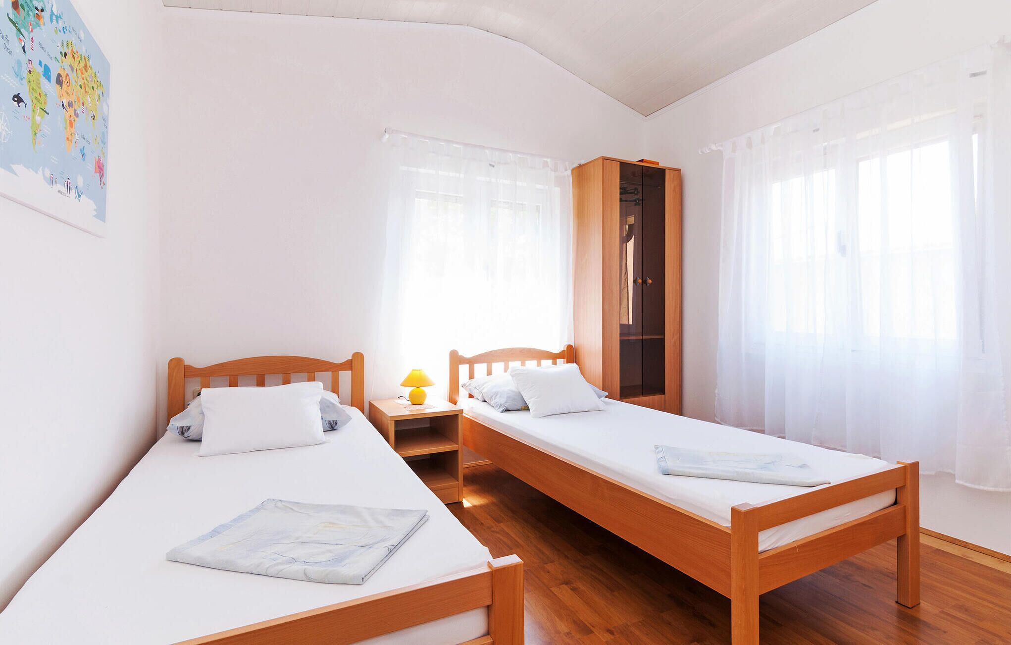 Une chambre avec deux lits en bois, une armoire et une carte accrochée au mur.