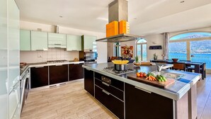 A modern kitchen with a central island, a stove, and a large window overlooking a scenic view. - Villa Panoramica, Menaggio, Italy (Menaggio)