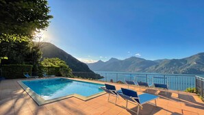 A swimming pool with lounge chairs, a tiled deck, and a view of mountains and a lake. - Villa Panoramica, Menaggio, Italy (Menaggio)