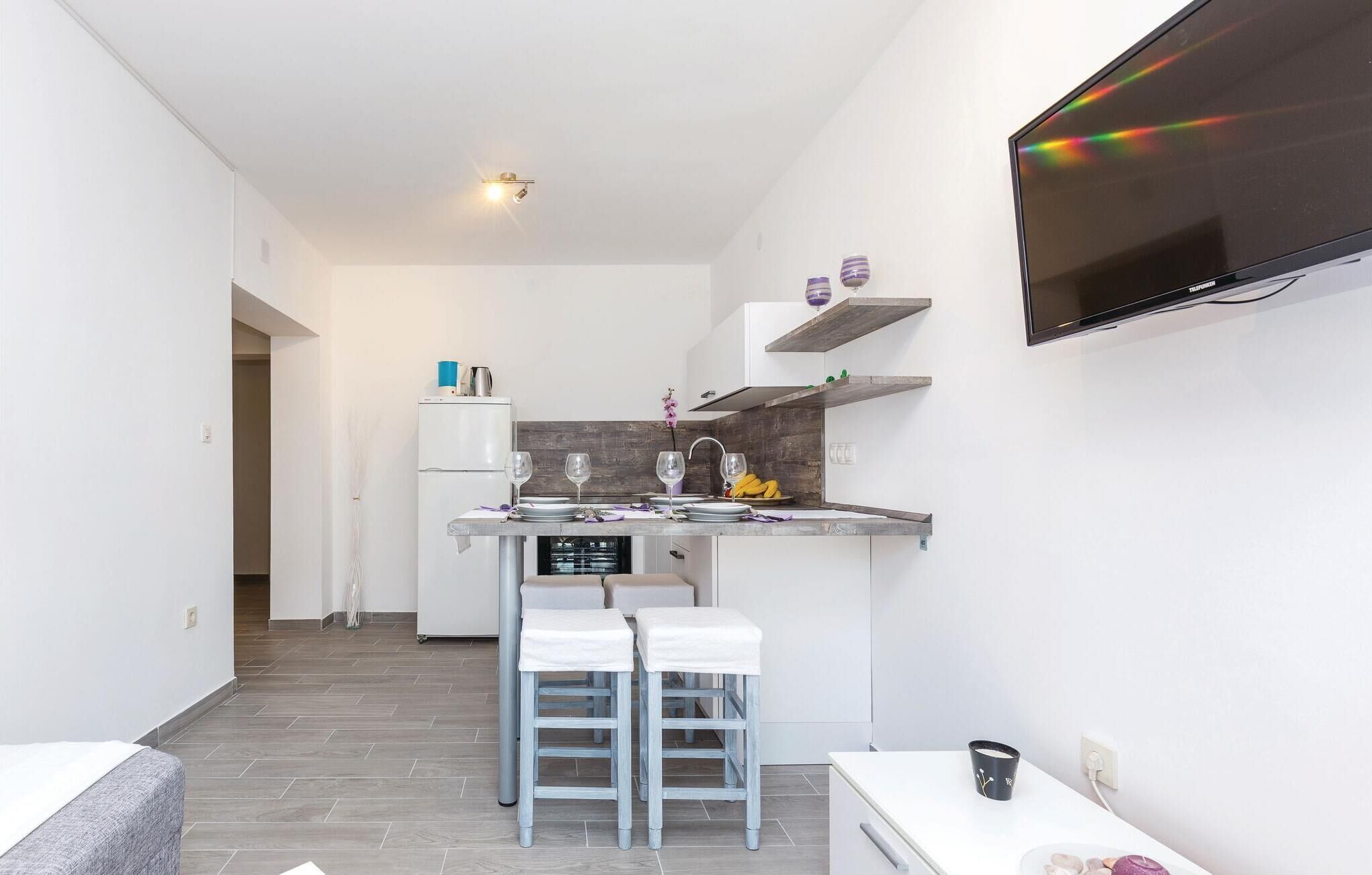 A compact kitchen with a built-in TV, a refrigerator, and a dining area with two stools.