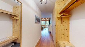 Ein Holzbodenkorridor mit einer Bank links, einem Bild an der Wand und Blick in einen Raum mit einer Bank und einem Tisch.